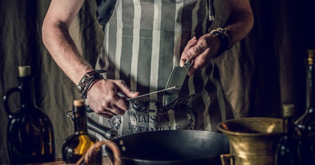 Crop faceless chef sharpening knives before preparing food in frying pan